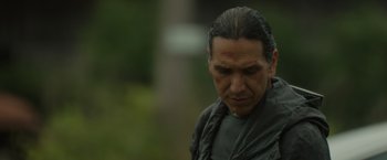 Movie still from “Firestarter” (2022), directed by Keith Thomas – An older man with long black hair is looking down at the ground; Close Up shot, Over the shoulder angle