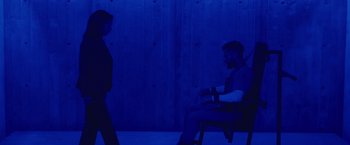 Movie still from “Firestarter” (2022), directed by Keith Thomas – A man sitting on a chair in front of another man; Wide shot, High angle