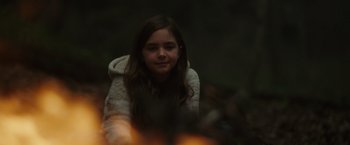 Movie still from “Firestarter” (2022), directed by Keith Thomas – A young girl sitting in front of a fire; Medium shot, Over the shoulder angle