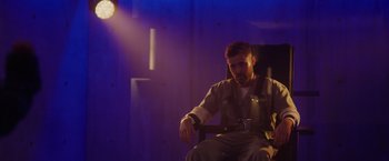 Movie still from “Firestarter” (2022), directed by Keith Thomas – A man sitting in a chair in front of a purple wall; Wide shot, Low angle