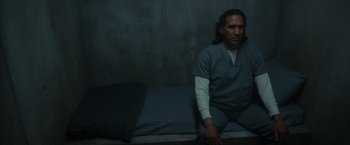Movie still from “Firestarter” (2022), directed by Keith Thomas – A man sitting on a bed in a jail cell; Medium shot, High angle