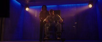 Movie still from “Firestarter” (2022), directed by Keith Thomas – A woman standing next to a man sitting in a chair; Wide shot, Low angle