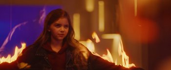 Movie still from “Firestarter” (2022), directed by Keith Thomas – A young girl is standing in front of a fire; Medium shot, Over the shoulder angle