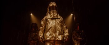 Movie still from “Firestarter” (2022), directed by Keith Thomas – A man in a gold suit standing in the dark; Medium shot, Low angle