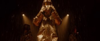 Movie still from “Firestarter” (2022), directed by Keith Thomas – A person in a gold suit and a helmet; Medium shot, Low angle