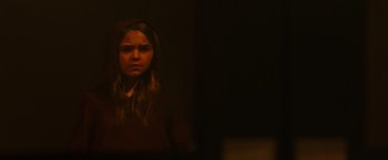 Movie still from “Firestarter” (2022), directed by Keith Thomas – A young girl is standing in a dark room; Close Up shot, Over the shoulder angle
