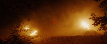 Movie still from “Firestarter” (2022), directed by Keith Thomas – A person standing in the distance in the dark with a car in the background; Extreme Wide shot, High angle