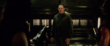 Movie still from “Alien: Resurrection” (1997), directed by Jean-Pierre Jeunet – A man standing next to a machine gun in a room; Medium shot, Low angle