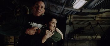 Movie still from “Alien: Resurrection” (1997), directed by Jean-Pierre Jeunet – A man holding a gun over a woman's shoulder; Medium shot, Low angle