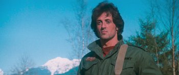 Movie still from “First Blood” (1982), directed by Ted Kotcheff – A man in a green jacket is standing in front of a tree; Close Up shot, Low angle