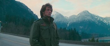 Movie still from “First Blood” (1982), directed by Ted Kotcheff – A man in a green jacket standing in front of mountains; Medium shot, Low angle