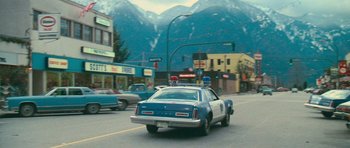 Movie still from “First Blood” (1982), directed by Ted Kotcheff – A police car driving down a street with mountains in the background; Wide shot, High angle