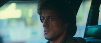 Movie still from “First Blood” (1982), directed by Ted Kotcheff – A man with long dark hair is sitting in a car; Close Up shot, Over the shoulder angle