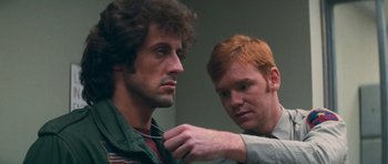Movie still from “First Blood” (1982), directed by Ted Kotcheff – A man helping another man fix his collar; Close Up shot, Over the shoulder angle