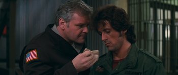 Movie still from “First Blood” (1982), directed by Ted Kotcheff – A man and a man holding a piece of food; Close Up shot, Over the shoulder angle