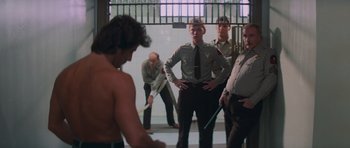 Movie still from “First Blood” (1982), directed by Ted Kotcheff – A group of men standing in front of each other in a jail cell; Wide shot, Over the shoulder angle