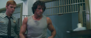 Movie still from “First Blood” (1982), directed by Ted Kotcheff – A man with long hair is standing in front of a wall; Medium shot, Over the shoulder angle