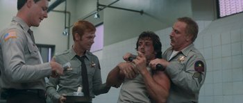 Movie still from “First Blood” (1982), directed by Ted Kotcheff – Three men in a bathroom one of them is holding a microphone; Medium shot, Over the shoulder angle