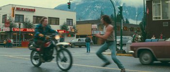 Movie still from “First Blood” (1982), directed by Ted Kotcheff – A man running across a street while a motorcycle passes by; Wide shot, Over the shoulder angle