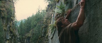 Movie still from “First Blood” (1982), directed by Ted Kotcheff – A man climbing up a rock wall with ferns growing on top of it; Close Up shot, Low angle