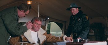 Movie still from “First Blood” (1982), directed by Ted Kotcheff – A man with a bandaged head is sitting in front of another man; Medium shot, Low angle