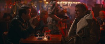 Movie still from “First Blood” (1982), directed by Ted Kotcheff – People are sitting at a table in front of a crowd of onlookers; Medium shot, Over the shoulder angle