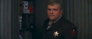 Movie still from “First Blood” (1982), directed by Ted Kotcheff – A man wearing a sheriff's badge stands in front of a wall; Close Up shot, Low angle