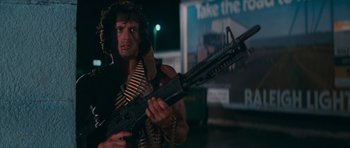 Movie still from “First Blood” (1982), directed by Ted Kotcheff – A man holding a gun in front of an advertisement; Medium shot, Low angle