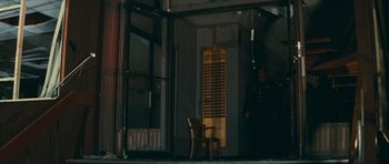 Movie still from “First Blood” (1982), directed by Ted Kotcheff – A person standing next to a chair in front of a building; Wide shot, Low angle