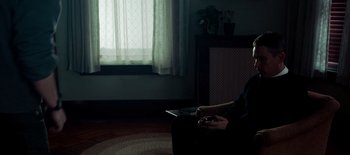 Movie still from “First Reformed” (2017), directed by Paul Schrader – A person sitting on a chair in a dark room; Medium shot, High angle