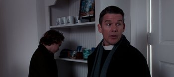 Movie still from “First Reformed” (2017), directed by Paul Schrader – A man standing in front of a shelf with cups; Medium shot, Over the shoulder angle