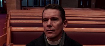 Movie still from “First Reformed” (2017), directed by Paul Schrader – A man in a priest's outfit sitting in a church; Close Up shot, Low angle