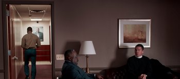 Movie still from “First Reformed” (2017), directed by Paul Schrader – A man sitting in front of a lamp in front of a painting; Wide shot, Over the shoulder angle