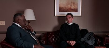 Movie still from “First Reformed” (2017), directed by Paul Schrader – Two men sitting on top of a red leather couch; Medium shot, Over the shoulder angle