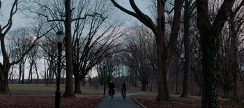 Movie still from “First Reformed” (2017), directed by Paul Schrader – Two bicyclists riding down a tree - lined path in a park; Extreme Wide shot, High angle