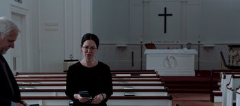 Movie still from “First Reformed” (2017), directed by Paul Schrader – A woman holding a cell phone standing in front of pews in a church; Medium shot, Low angle