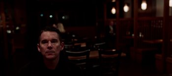 Movie still from “First Reformed” (2017), directed by Paul Schrader – A man sitting at a table in front of a group of people; Close Up shot, Over the shoulder angle