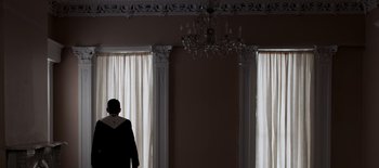 Movie still from “First Reformed” (2017), directed by Paul Schrader – A person standing in front of a window with a chandelier; Wide shot, Low angle