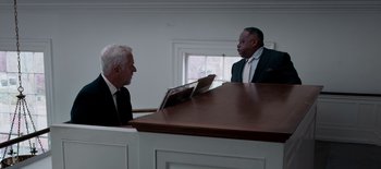 Movie still from “First Reformed” (2017), directed by Paul Schrader – Two men in business suits sitting in front of a wooden desk; Medium shot, High angle
