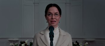 Movie still from “First Reformed” (2017), directed by Paul Schrader – A woman wearing glasses and a white jacket is holding a microphone in front of her face; Close Up shot, Low angle