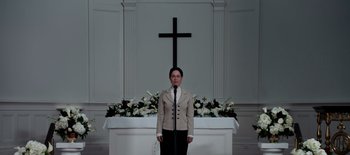 Movie still from “First Reformed” (2017), directed by Paul Schrader – A man standing in front of a cross and a podium; Medium shot, Low angle