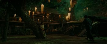 Movie still from “Fistful of Vengeance” (2022), directed by Roel Reiné – A man sitting on top of a tree in front of a building; Extreme Wide shot, High angle