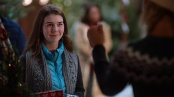 Movie still from “Fit for Christmas” (2022), directed by Jessica Harmon – A girl is smiling while a person is holding something up; Close Up shot, Over the shoulder angle