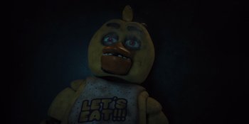 Movie still from “Five Nights at Freddy's” (2023), directed by Emma Tammi – A yellow stuffed animal with a face that says " let's eat " on it's chest; Close Up shot, High angle