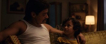 Movie still from “Flamin' Hot” (2023), directed by Eva Longoria – A man sitting next to a young girl on a couch; Medium shot, Over the shoulder angle