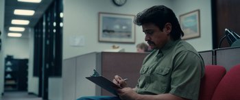 Movie still from “Flamin' Hot” (2023), directed by Eva Longoria – A man writing on a clipboard while sitting in a room; Medium shot, Over the shoulder angle