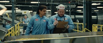 Movie still from “Flamin' Hot” (2023), directed by Eva Longoria – Two men are working in an industrial kitchen; Medium shot, Low angle