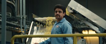 Movie still from “Flamin' Hot” (2023), directed by Eva Longoria – A man standing in front of a conveyor belt; Close Up shot, Low angle
