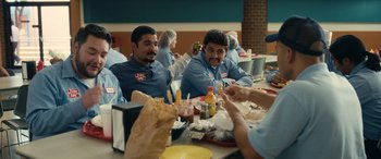 Movie still from “Flamin' Hot” (2023), directed by Eva Longoria – A group of men sitting at a table eating food; Medium shot, Over the shoulder angle