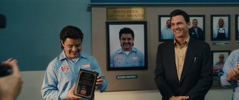 Movie still from “Flamin' Hot” (2023), directed by Eva Longoria – A man standing next to another man holding an employee of the month plaque; Medium shot, Over the shoulder angle